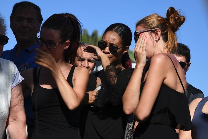 People cry as they stand next to the makeshift memorial where people laid flowers in tribute to those killed in Nice, France.