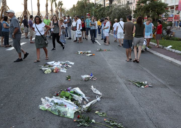 People pass flowers and messages left in the road for victims of the deadly Bastille Day attack.