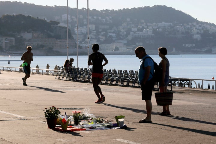 A couple watch flowers placed in tribute to one of the victims at the scene of a deadly attack while joggers pass by.