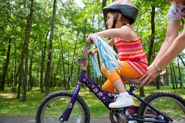 Mother helping daughter to ride bicycle Image Source via Getty Images