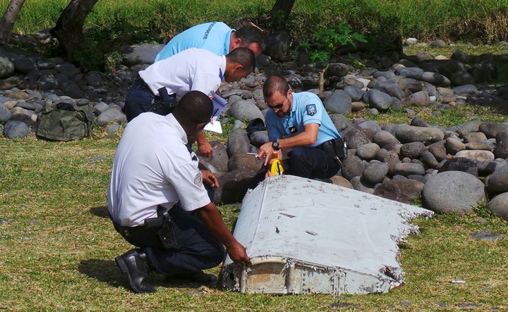 French gendarmes and police inspecting a large piece of plane debris which was found on the beach on the French Indian Ocean island of La Reunion in 2015