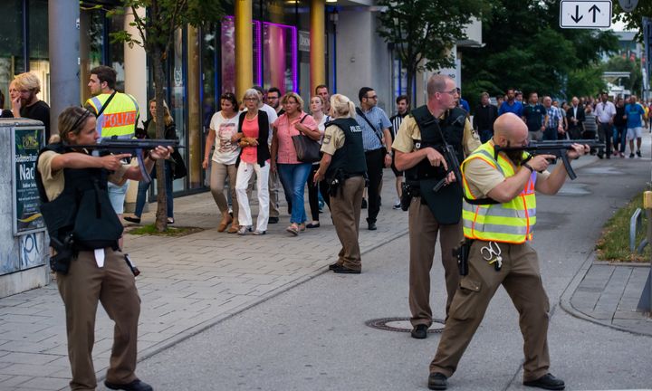 Police officers guard with guns as other officers escort people from inside the shopping center as they respond to the shooting at the Olympia Einkaufzentrum on Friday