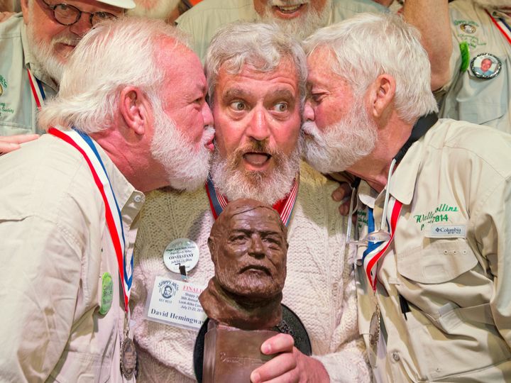 Dave Hemingway receives smooches from Charlie Boise, left, and Wally Collins, right, after winning the 2016 Ernest "Papa" Hemingway Look-Alike Contest in Key West, Florida on July 23, 2016.