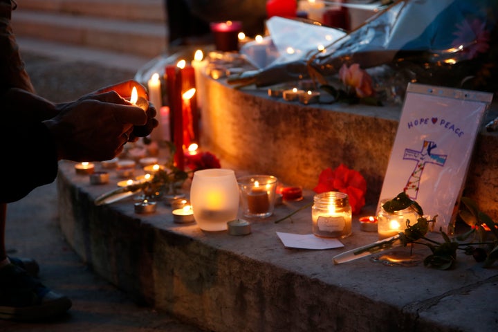 A woman lights a candle to place with flowers and candles at the town hall in Saint-Etienne-du-Rouvray, near Rouen in Normandy, France.