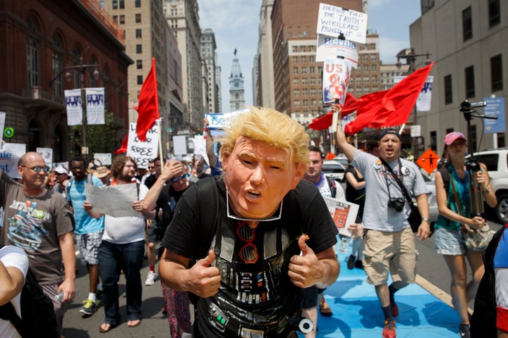 A man wears a Donald Trump face mask as people march holding signs in support of Bernie Sanders during a protest at the Democ