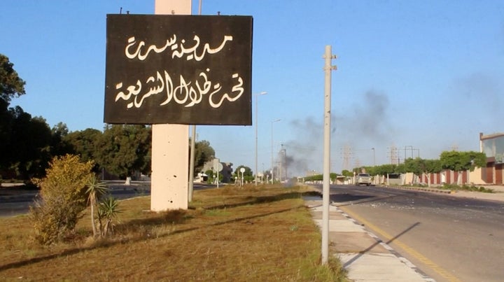 A sign which reads in Arabic, "The city of Sirte, under the shadow of Sharia" is seen as smoke rises in the background in Jun