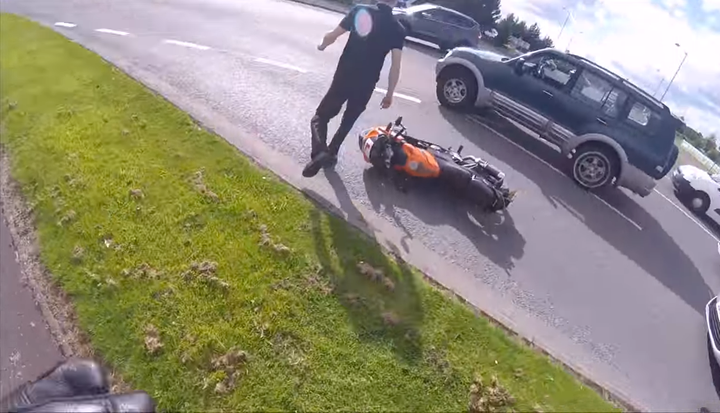 The motorist walks back to his vehicle after shoving the motorcyclist to the ground