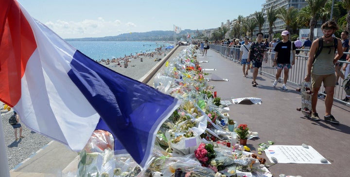 People walk past flowers left in tribute at a makeshift memorial to the victims of the Bastille Day truck attack near the Pro