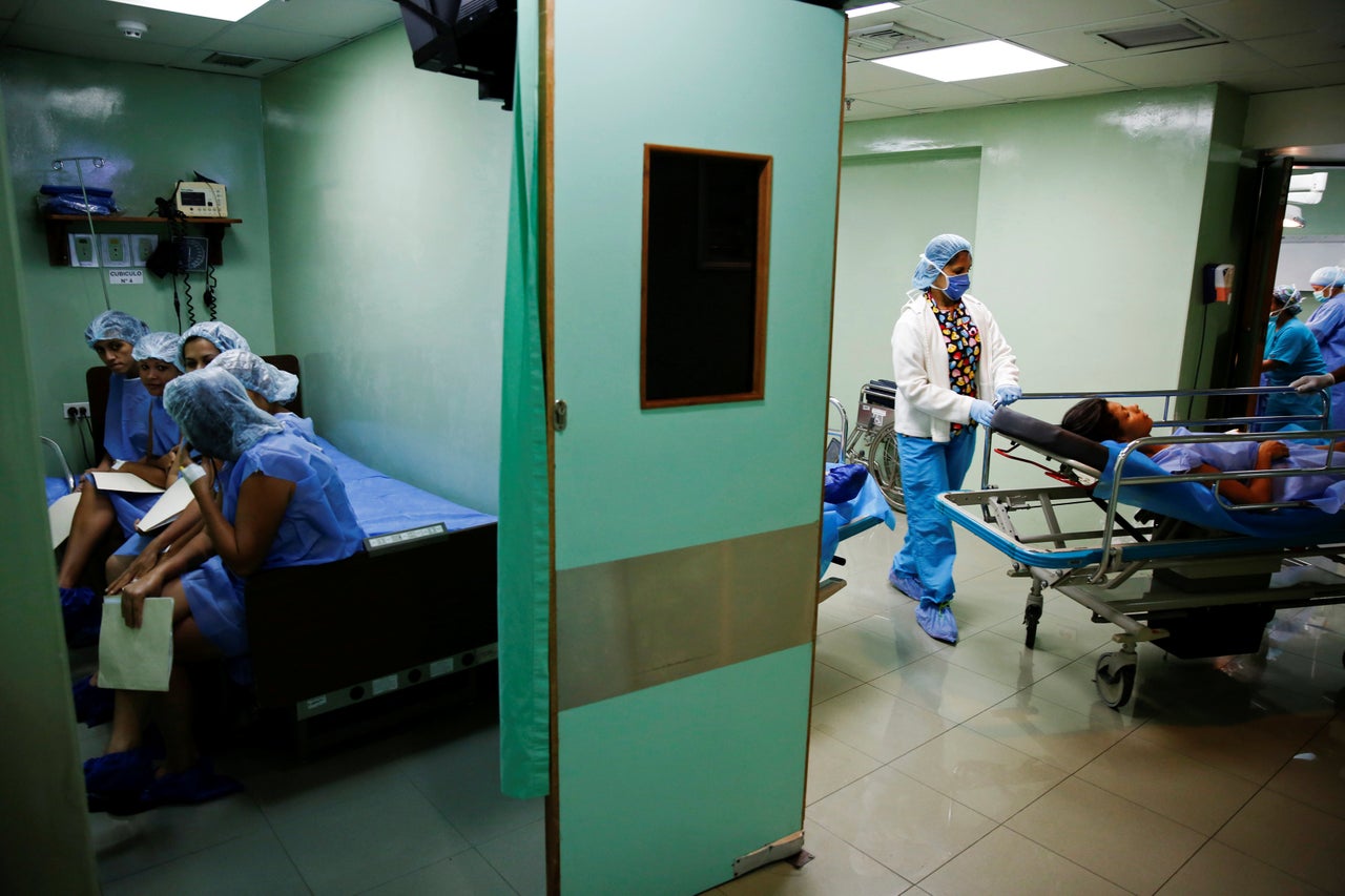 Medical personnel move a woman after her sterilization surgery, as other women are waiting for the procedure.