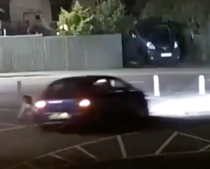 The car drives at the man for a second time, but he is able to move out of the way.