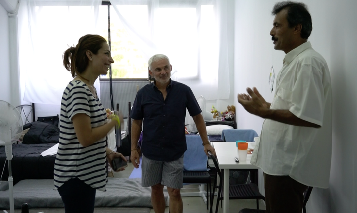 A Syrian refugee stands in one of Elpida's rooms speaking with co-founder Frank Giustra, of The Radcliffe Foundation, and Sandy Hakim, Elpida's chief community liaison.