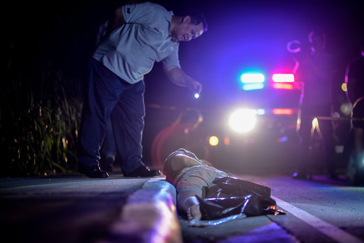 A member of the police's homicide division inspects the corpse of a suspected drug addict and victim of a vigilante-style execution with his hands tied and head wrapped with tape on a street in Manila, Philippines, July 27, 2016.