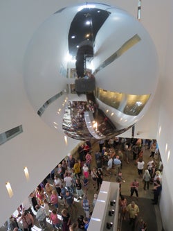 The Trevor Paglen Orbital Reflector suspended above Tilting the Basin opening reception guests in the Donald W. Reynolds Grand Hall .