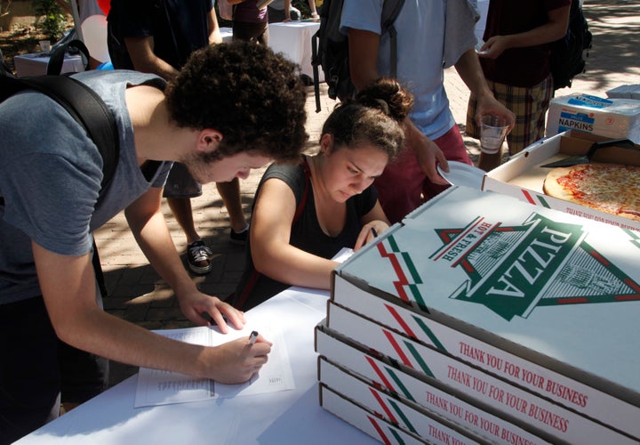 College of Charleston students fill out a voter registration form while waiting in line for a slice of pizza at a Rock The Vo