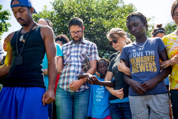 People link arms during a group prayer across the street from a gas station on Aug. 14, 2016 in Milwaukee, Wisconsin. The gas station was destroyed in protests the day before.