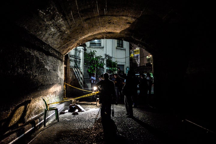 Police and media inspect the corpse of a suspected drug pusher and victim of a vigilante-style execution under a bridge in Ma
