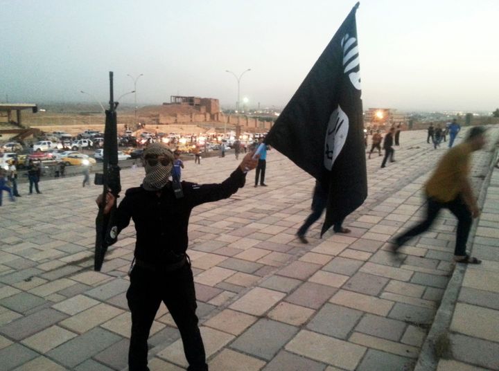 An IS fighter brandishes a flag and a weapon on a street in the city of Mosul in 2014 