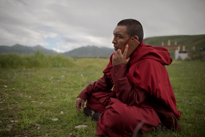 A Tibetan Buddhist monk talks on his smartphone as he sits on the grassland of the Tibetan Plateau in Yushu County.