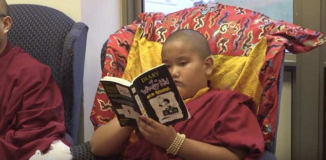 Jalue Dorje reads "Diary of a Wimpy Kid" during a Tibetan Buddhist ceremony.