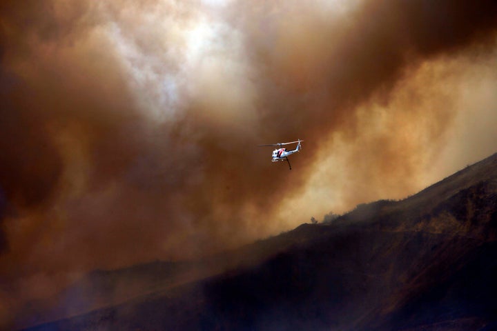 A firefighting helicopter maneuvers around power lines and smoke to make a water drop during the Blue Cut fire at the Cajon Pass in San Bernardino County, California.