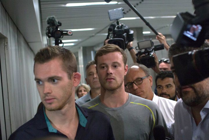 Journalists surround American Olympic swimmers Gunnar Bentz, left, and Jack Conger, center, as they leave the police station at Rio International airport.