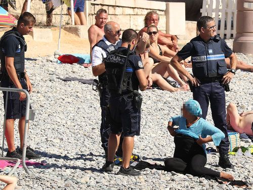 Police apprehend a woman on the beach for wearing body-covering swimwear on the Promenade des Anglais beach in Nice, France on August 23, 2016.
