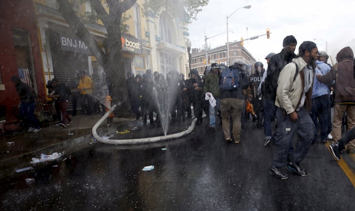 A fire hose cut by Baltimore protesters sprays water into the air as a line of police move toward a burning CVS drug store after Freddie Gray's funeral on April 27, 2015.