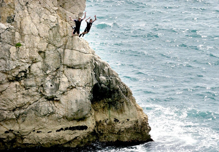 Two men jump off rocks into the sea at Durdle Door near West Lulworth, Dorset.