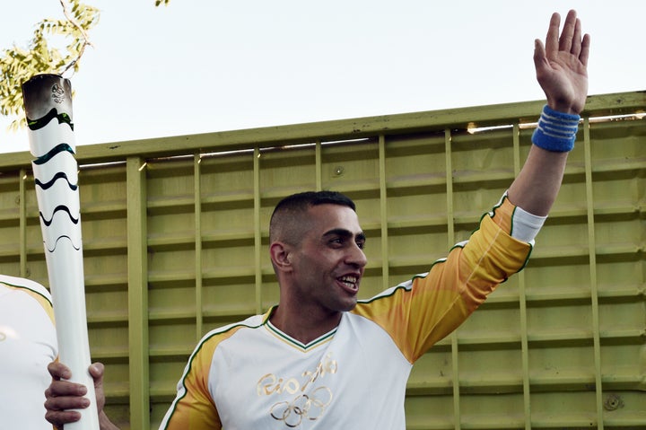 Syrian refugee and amputee swimmer Ibrahim Al-Hussein greets refugees as the Olympic Flame torch relay passes through the Ele