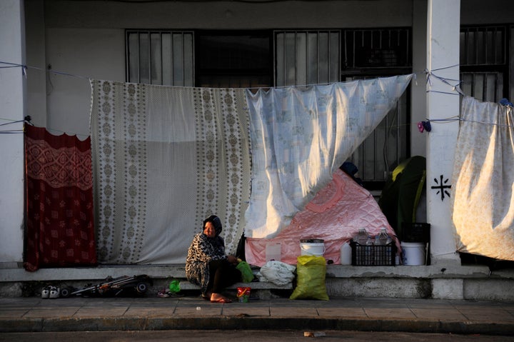 A woman sits outside a building covered with sheets to protect the dwellers from the strong summer sun outside of the Ellinik