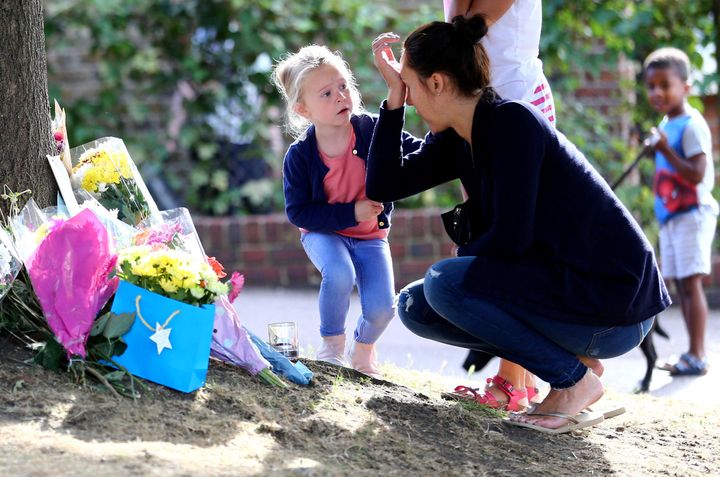 A woman is comforted by a child as she lays flowers at the scene