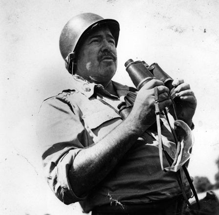 Ernest Hemingway in uniform, wearing a helmet, and holding binoculars during World War II, circa 1944.