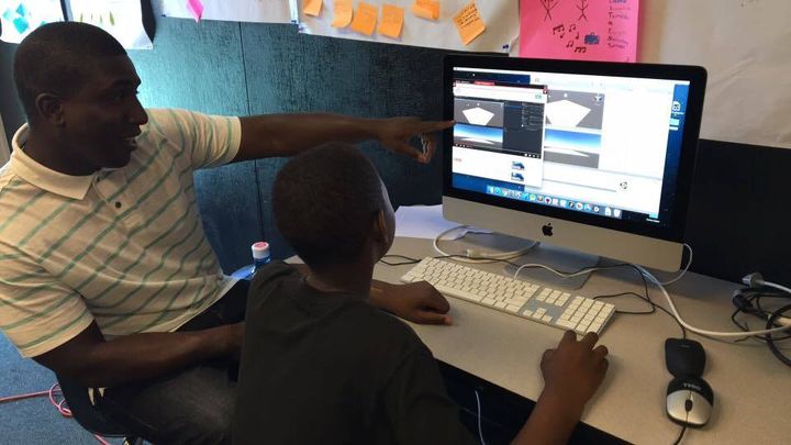 Stanford Ph.D. candidate and lead instructor Kareem Edouard discussing design methodology while his student uses one monitor to watch a YouTube coding tutorial and another monitor to code.