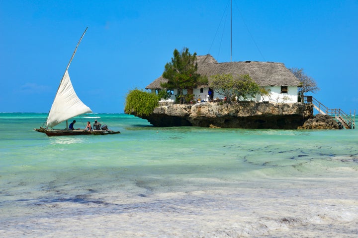 Tourist take a traditional Dhow boat to The Rock Restaurant just off Zanzibar's idyllic Bwejuu Beach.