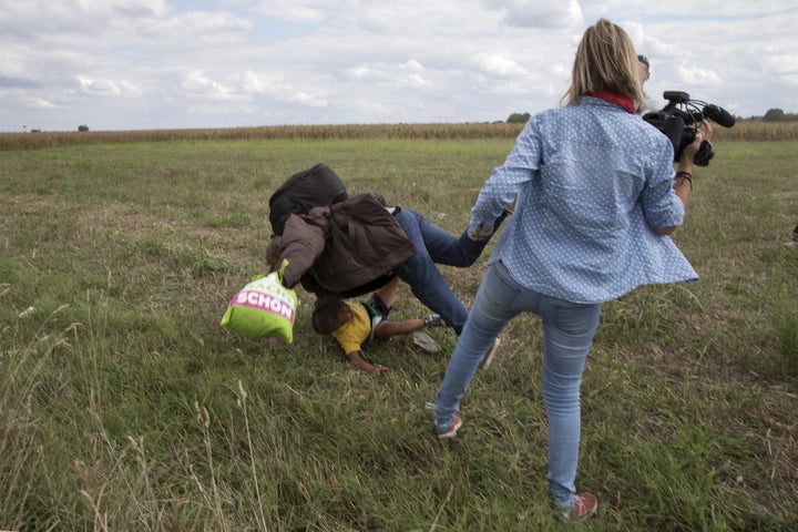 A migrant carrying a child falls near TV camerawoman (R) Petra Laszlo while trying to escape from a collection point in Roszke village, Hungary, September 8, 2015.