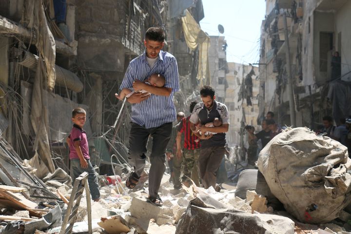 Syrian men carrying babies make their way through the rubble of destroyed buildings following a reported air strike on the rebel-held Salihin neighbourhood of the northern city of Aleppo, on September 11, 2016.