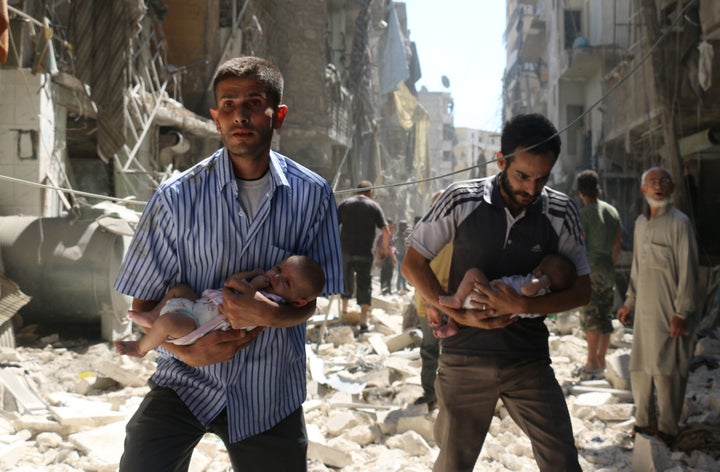 Syrian men carry&nbsp;babies through the rubble of destroyed buildings following a reported air strike on rebel-held Aleppo o