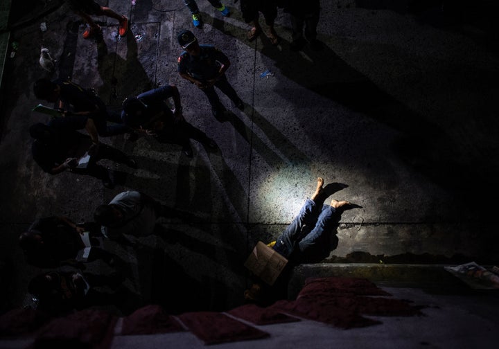 Police look at the dead body of an alleged drug dealer, his face covered with packing tape and a placard reading