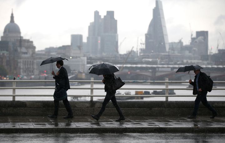 Commuters shelter under umbrellas as they cross Waterloo bridge during heavy rain in London on Friday