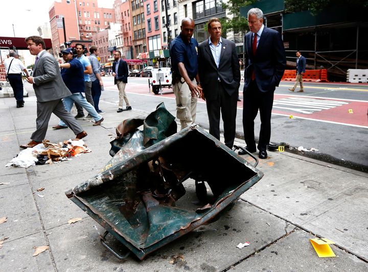New York Mayor Bill de Blasio (R) and New York Governor Andrew Cuomo (2-R) look over a mangled dumpster at the bomb site