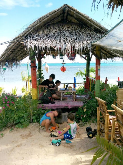 Paul and Caroline King work on laptops by beach in Koh Samui, Thailand while Winston and Henry play with toys on the sand.