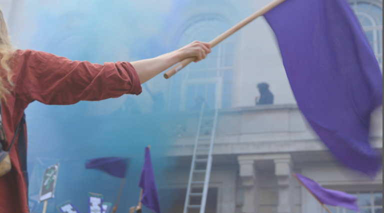 One Sisters Uncut protester waves a purple flag as activists climb onto Hackney Town Hall balcony. 