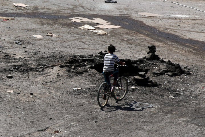 A boy rides a bicycle near a hole in the ground after an airstrike on Sunday in the rebel-held town of Dael, in Deraa Governo