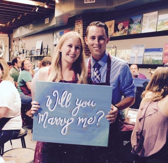 The happy couple posing with the "Will you marry me?" painting.