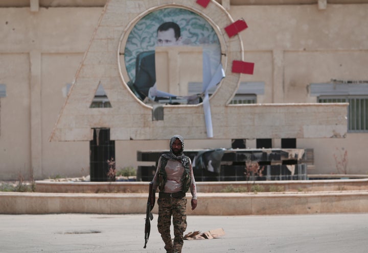 A YPG fighter in Kurd-controlled Hasaka, Syria, with a defaced picture of Syrian dictator Bashar Assad in the background. Though Assad avoided direct clashes with the Syrian Kurds for years, tensions between the YPG and the regime have grown in recent months and the Kurds have historically felt targeted by the Assads.