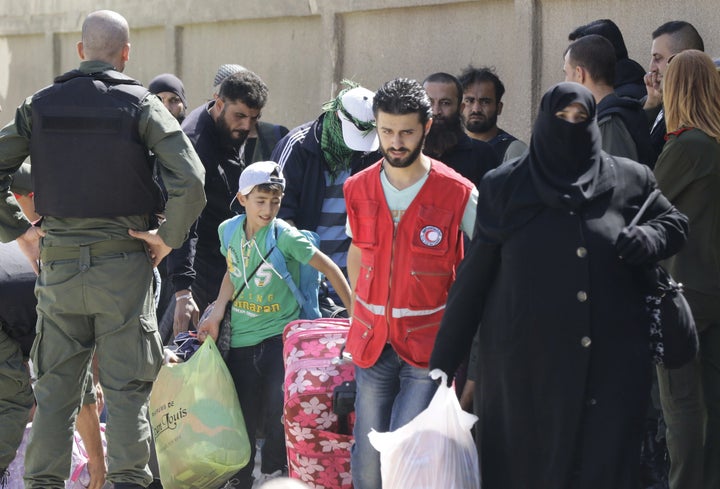 Syrian army and police forces stand guard as members of the Red Crescent help the families of opposition fighters evacuate at a Syrian army checkpoint in Homs on Thursday.