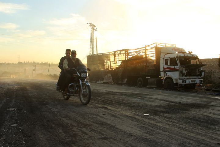 Men drive a motorcycle near a damaged aid truck after an airstrike on the rebel-held Urm al-Kubra town, western Aleppo city, Syria on September 20, 2016.