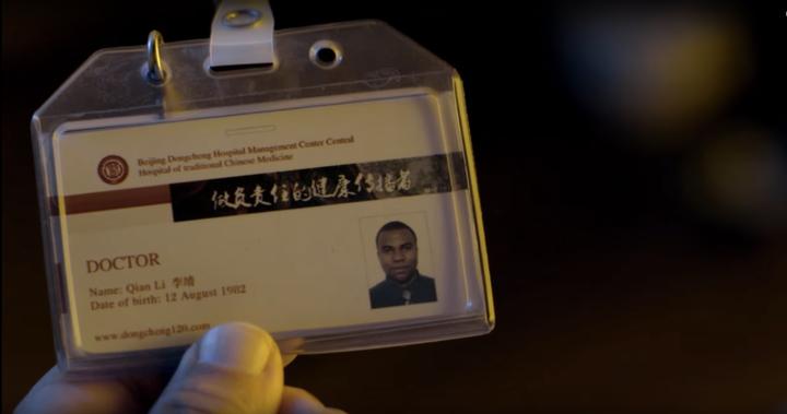 A Chinese man holds up the identification card of an African doctor working and living in China. The image is from Carl Houston Mc Millan's film "Laisuotuo."