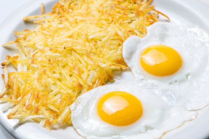 Hash browns sitting next to two eggs on a plate.