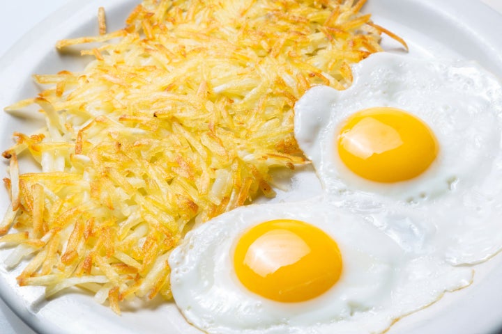 Hash browns sitting next to two eggs on a plate.